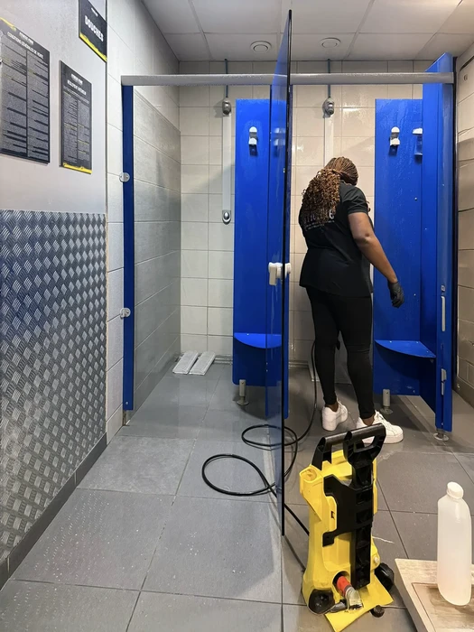 Femme en tenue de nettoyage professionnelle désinfecte un bureau moderne avec spray et chiffon, portant masque FFP2 et gants jaunes