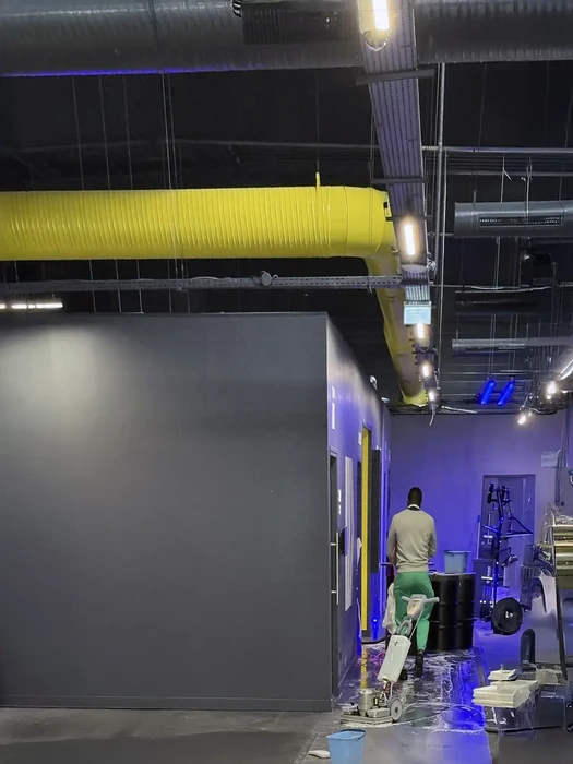 Personne en blouse bleue et gants nitrile violets effectuant le nettoyage d'un bureau blanc avec chiffon microfibre rose et spray désinfectant